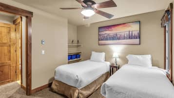 A hotel room with two beds, a ceiling fan, a painting of a winter landscape, and a wooden door.