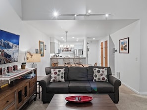 Una sala de estar moderna con un sofá, una zona de comedor con sillas y una cocina al fondo.