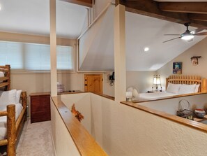 Un dormitorio con cabecera de madera, cama con ropa blanca, mesita de noche de madera y ventilador de techo.
