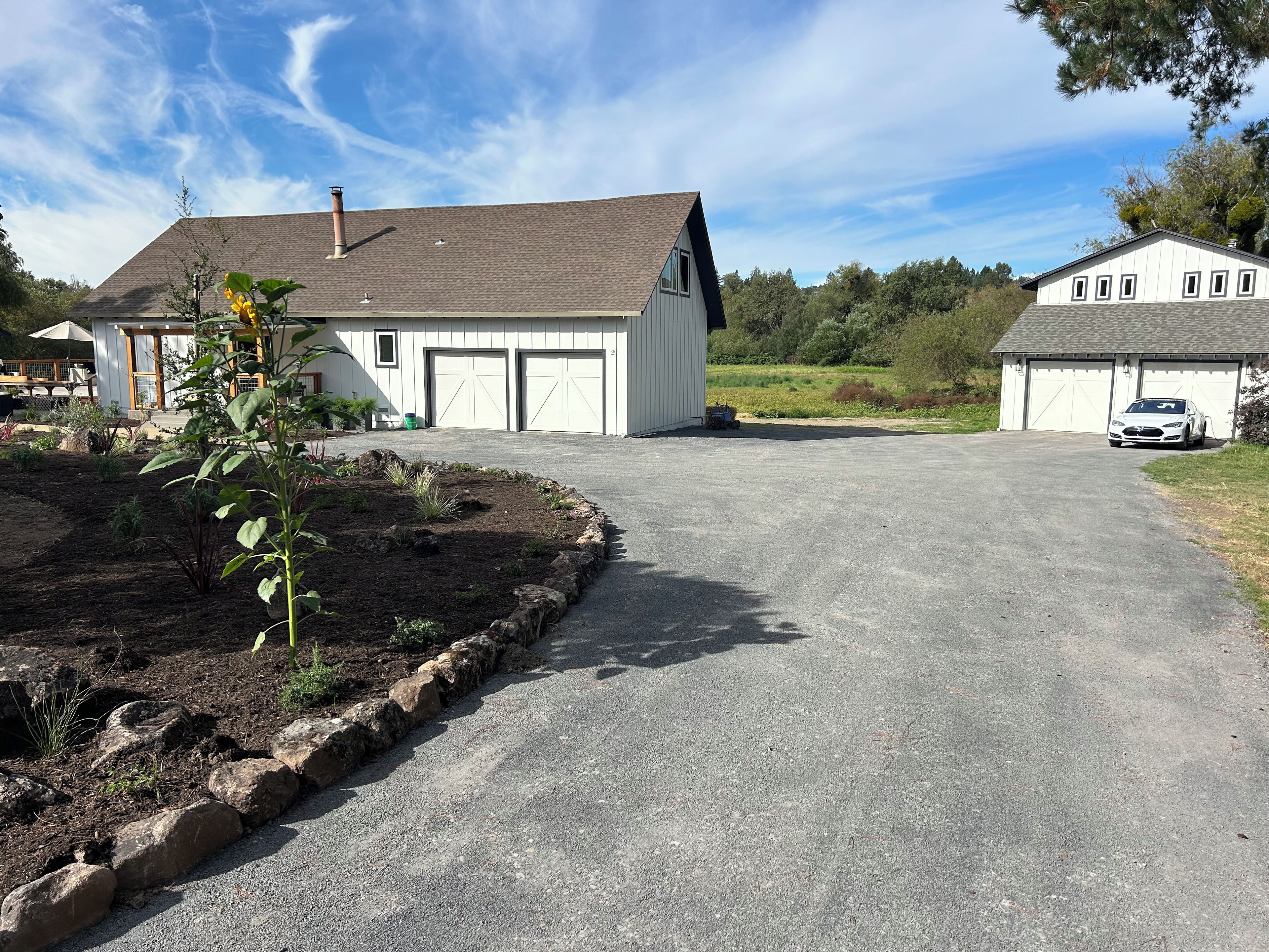 Een oprit naar een huis met garage, een tuin met planten en een geparkeerde auto.
