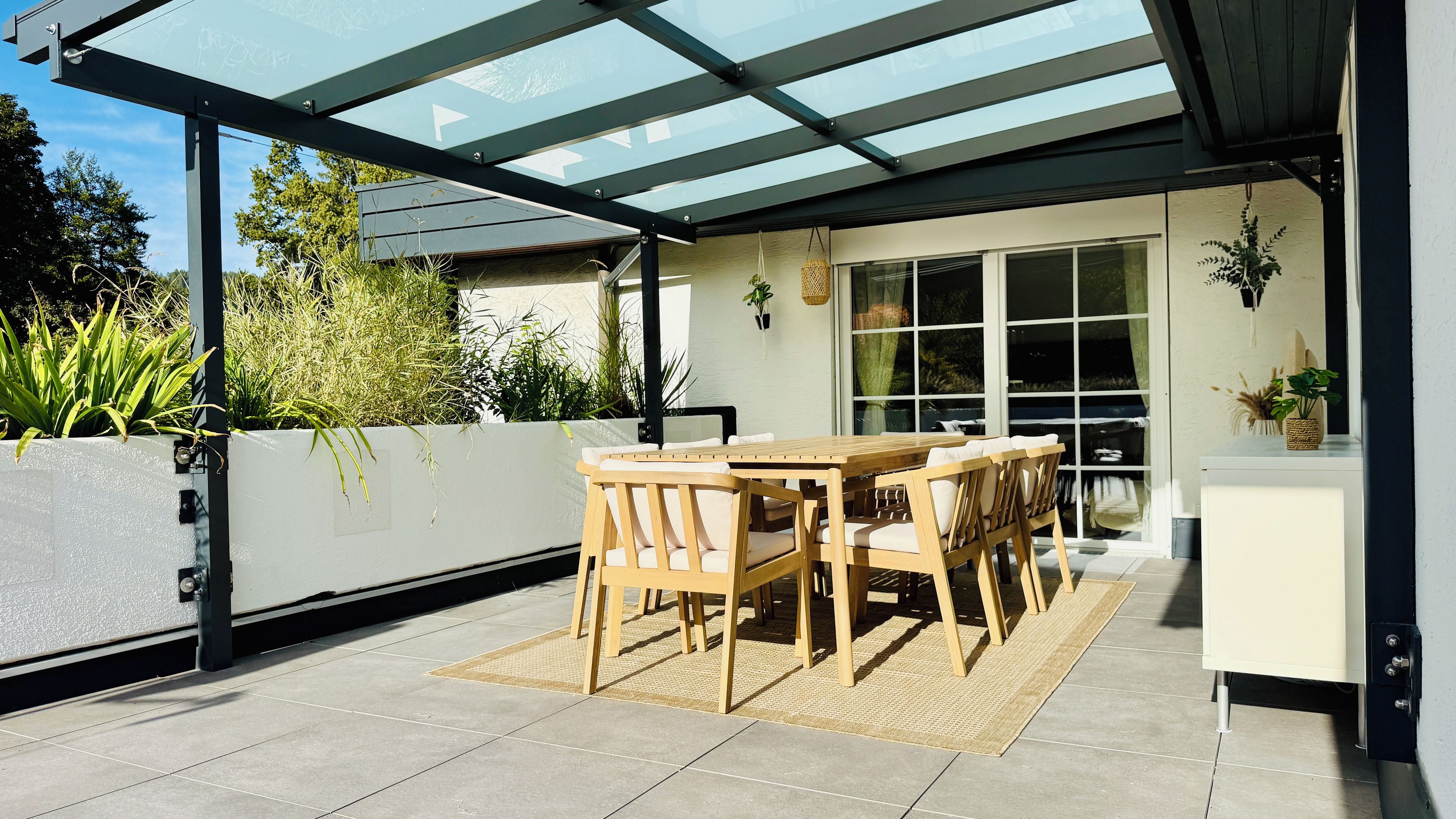 Une terrasse extérieure dotée d’un toit en verre, d’une table et de chaises en bois, ainsi que de plantes en pot.