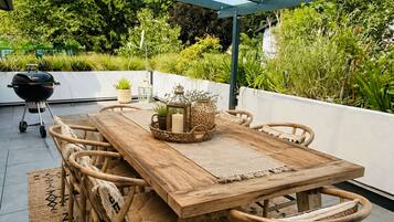 Un'area pranzo all'aperto con tavolo e sedie in legno, una pergola chiusa con vetro e un barbecue.
