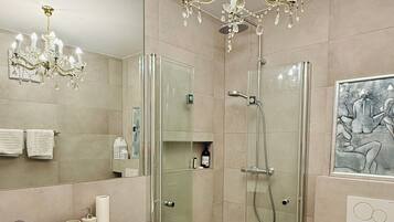 Un bagno moderno con un grande specchio, un mobile lavabo bianco, cabina doccia in vetro e un lampadario.