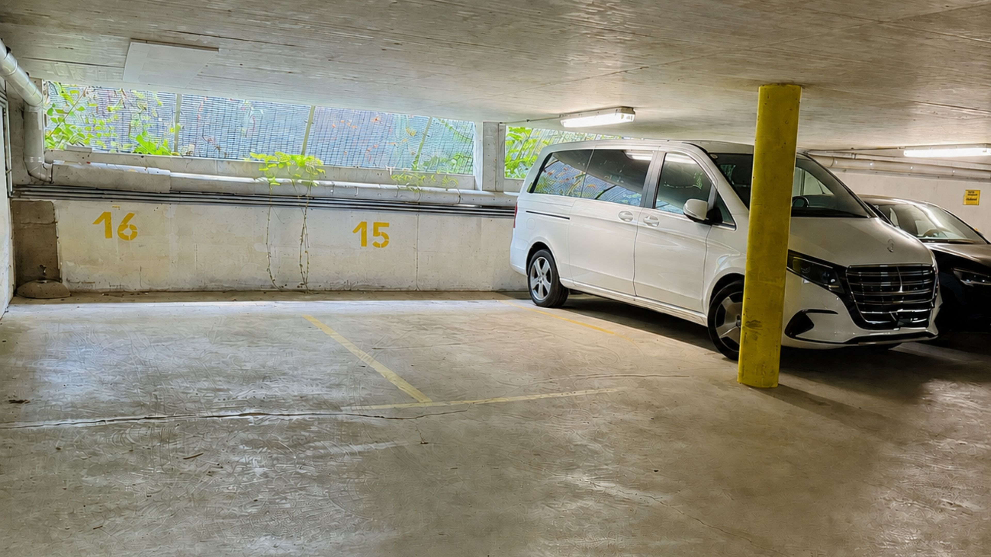 Eine Parkgarage mit Betonböden, nummerierten Stellplätzen und einem weißen Van, der auf Platz 15 geparkt ist.