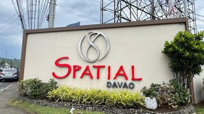A sign for 'Spatial Davao' with a logo, surrounded by greenery and a road with cars.