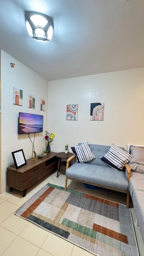 Un salon comprenant un canapé, un téléviseur à écran plat, un meuble en bois et des œuvres d’art abstraites accrochées au mur.