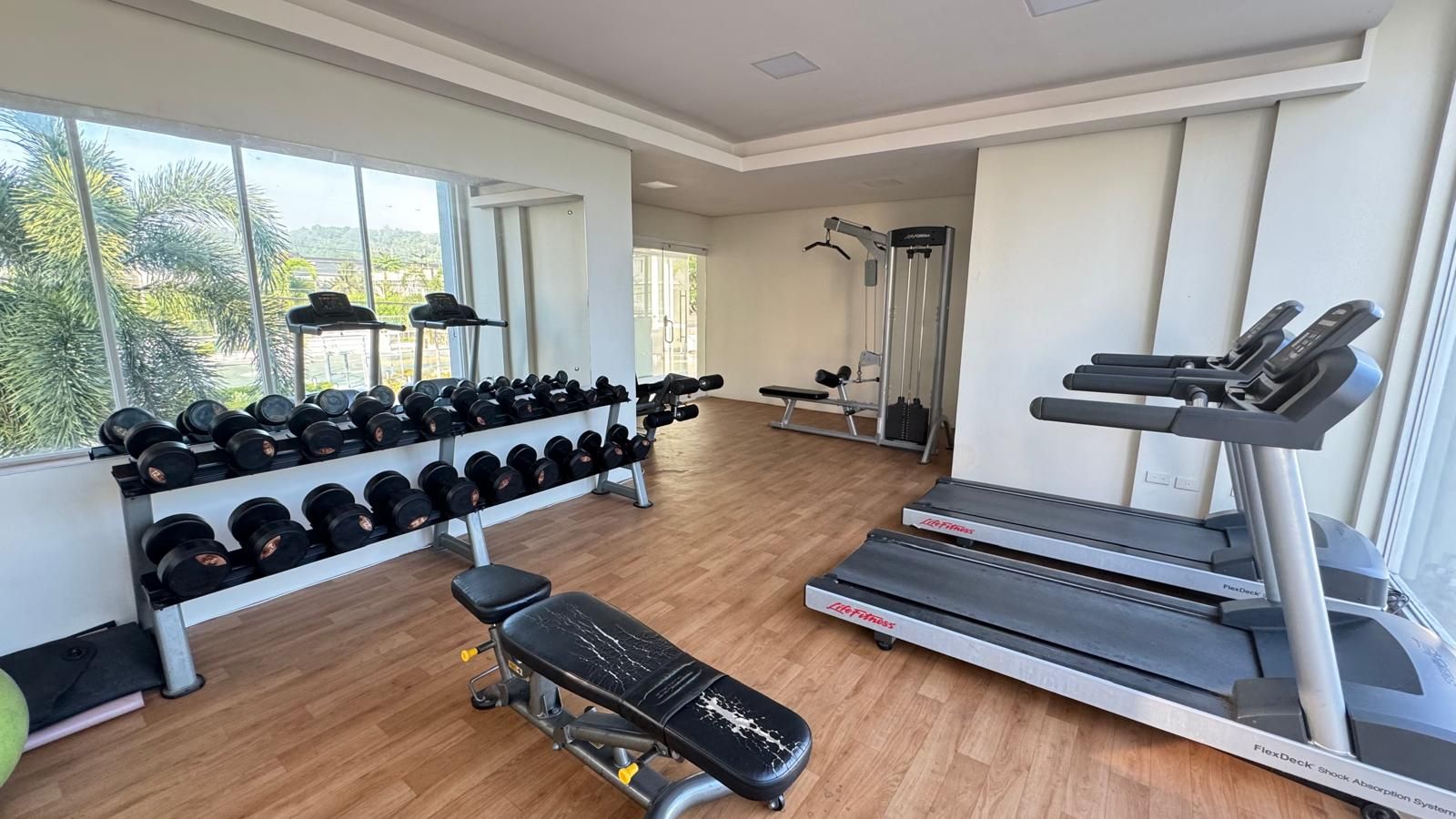 Une salle de sport équipée de tapis de course, d’haltères et de bancs de musculation.