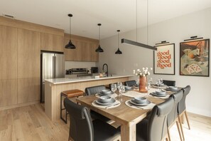 Une cuisine moderne avec des meubles en bois, un four encastré et un coin repas doté d’une table en bois, mise pour six personnes.