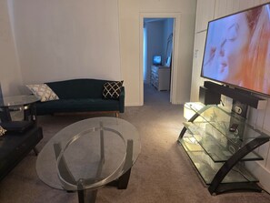 Ein Wohnzimmer mit einem grünen Sofa, einem Glastisch und einem Flachbildfernseher.