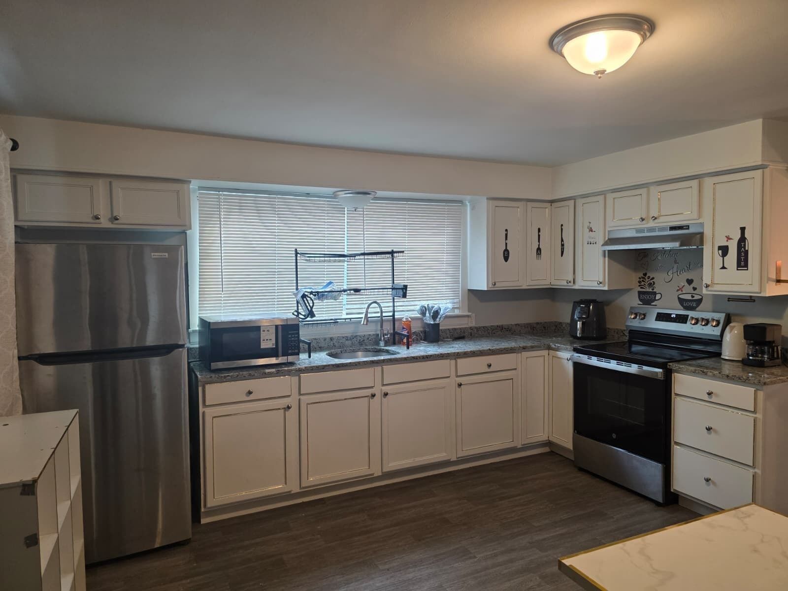 A modern kitchen with stainless steel appliances, white cabinetry, and a window with blinds.