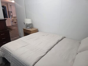 Een slaapkamer met een bed, nachtkastje, lamp en kledingkast.