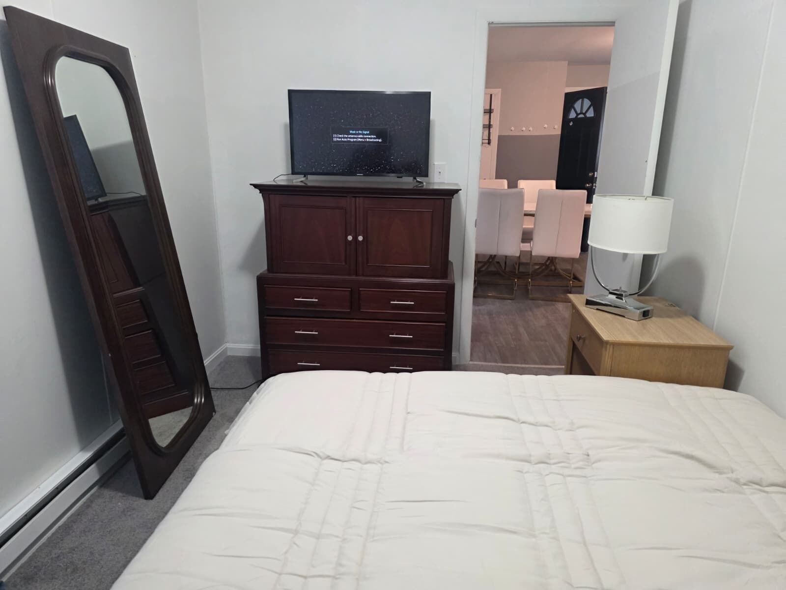 A hotel room with a bed, a dresser, a television, and a nightstand with a lamp.