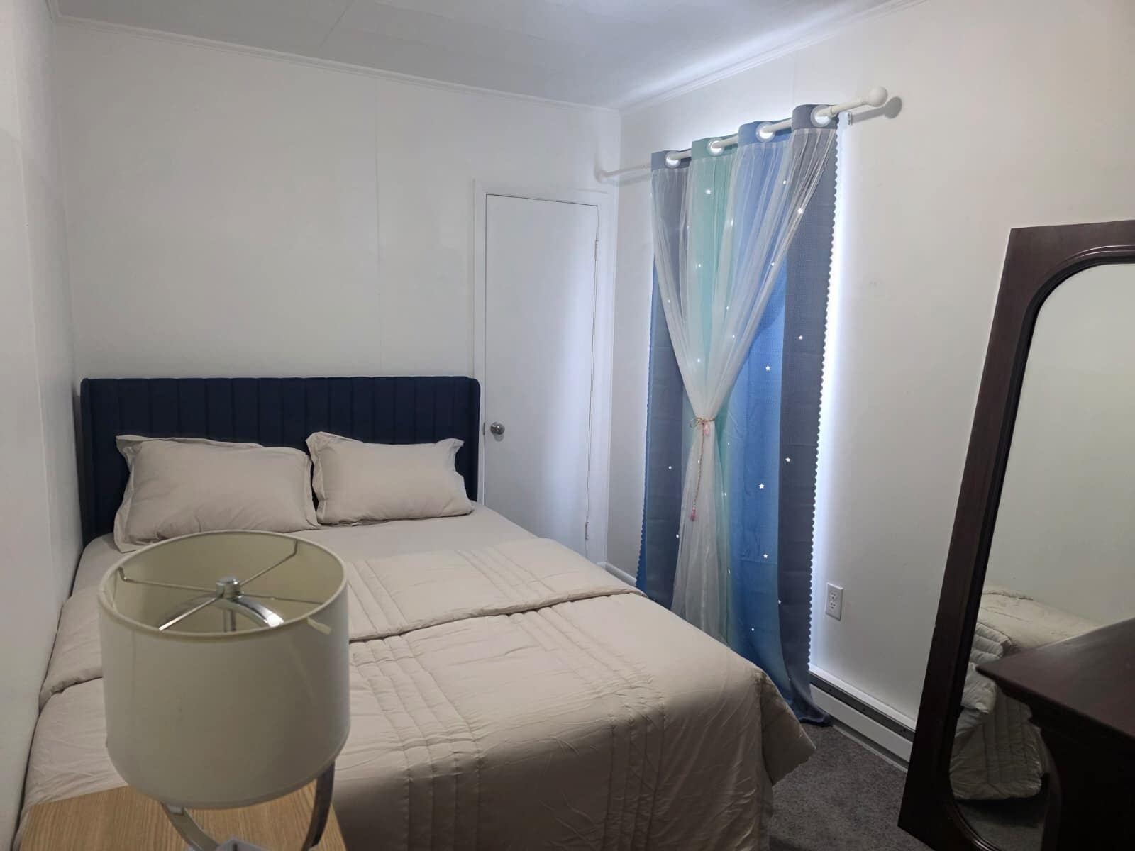 Une chambre à coucher avec un lit, une lampe de chevet, un rideau et un miroir.