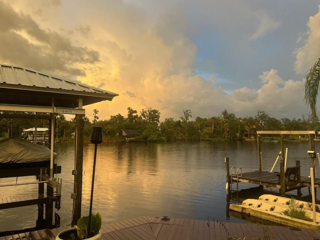 A dock with a covered seating area and a boat, surrounded by calm water and trees.