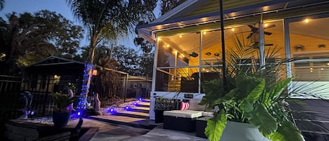 A modern house with a glass facade, a patio with outdoor seating, and a large potted plant in the foreground.