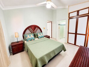 Ein Schlafzimmer mit einem Bett, Nachttischen, einer Lampe, einem Deckenventilator und einer Schiebetür.