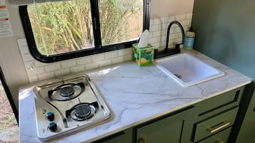 A compact kitchenette with a gas stove, a sink, and a window with a view of greenery.