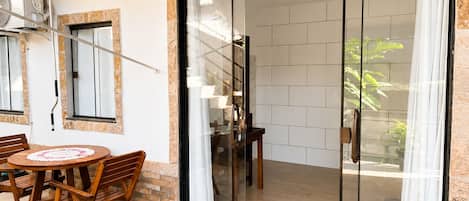 A modern outdoor seating area with a table and chairs, a sliding glass door leading to a tiled interior, and an air conditioning unit mounted on the wall.