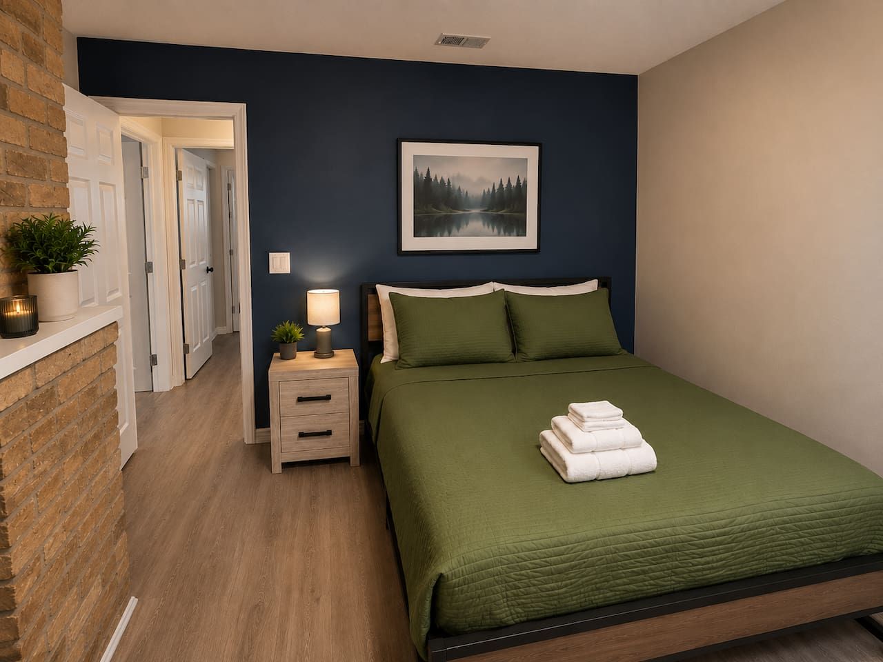 A bedroom with a bed, bedside table, lamp, and a framed picture on the wall.