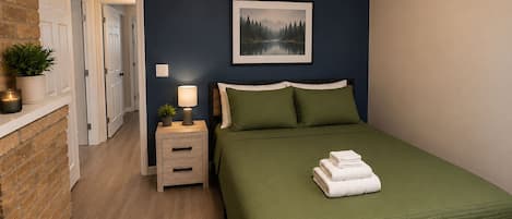 A bedroom with a bed, bedside table, lamp, and a framed picture on the wall.