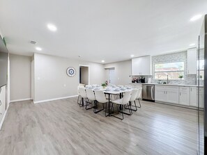 Eine moderne Küche mit weißen Schränken, einem Edelstahl-Kühlschrank und einem Essbereich mit rundem Tisch und Stühlen.