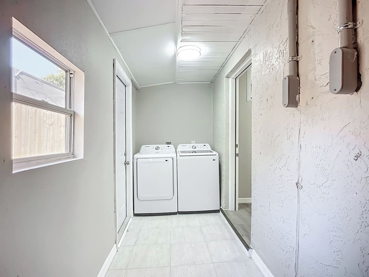 Un cuarto de lavandería con dos secadoras blancas, una ventana y una puerta.