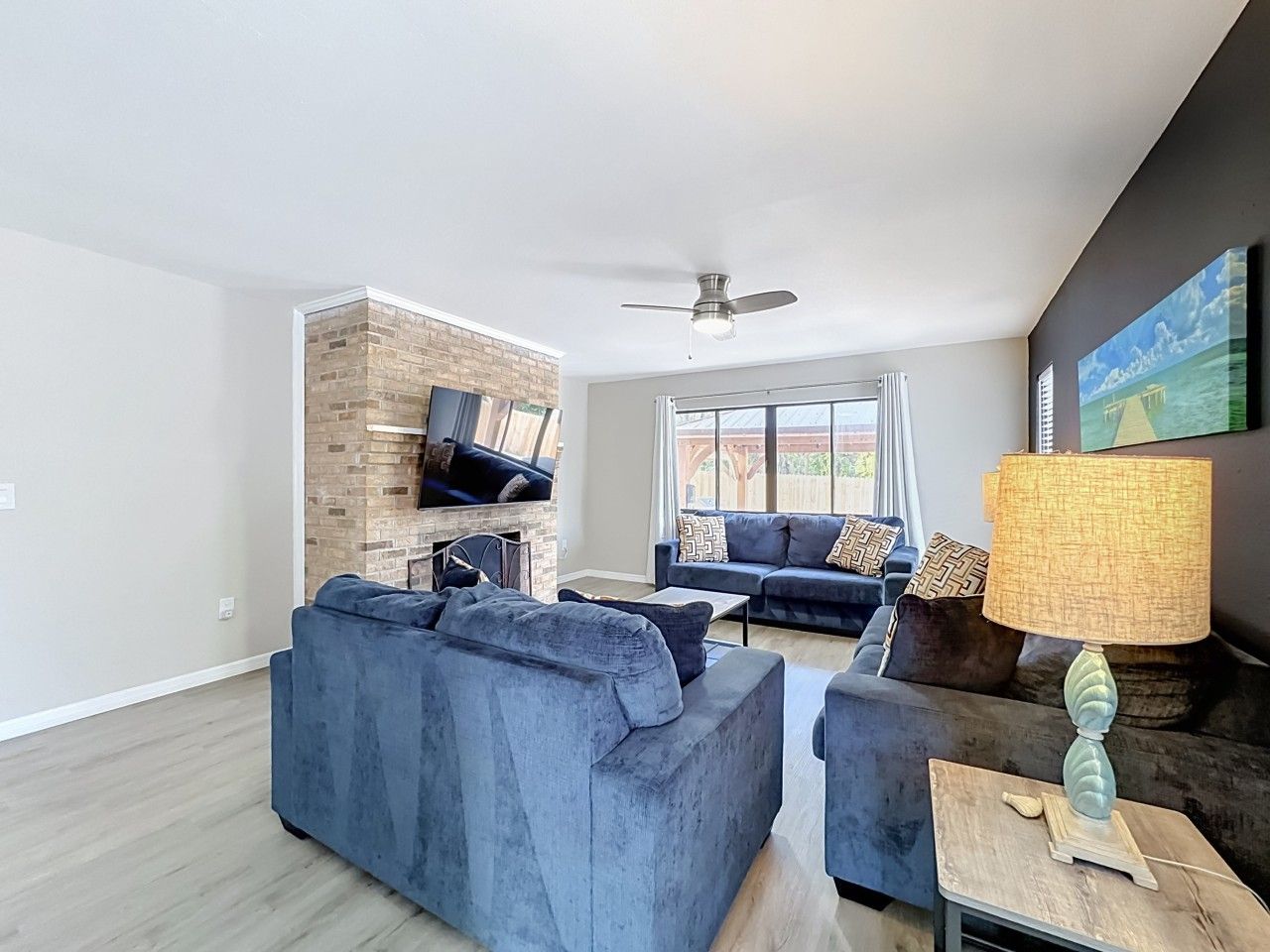 A modern living room with a brick fireplace, two sofas, a ceiling fan, and a television.