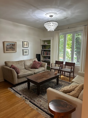 A living room with a sofa, a coffee table, a bookshelf, and a window with curtains.