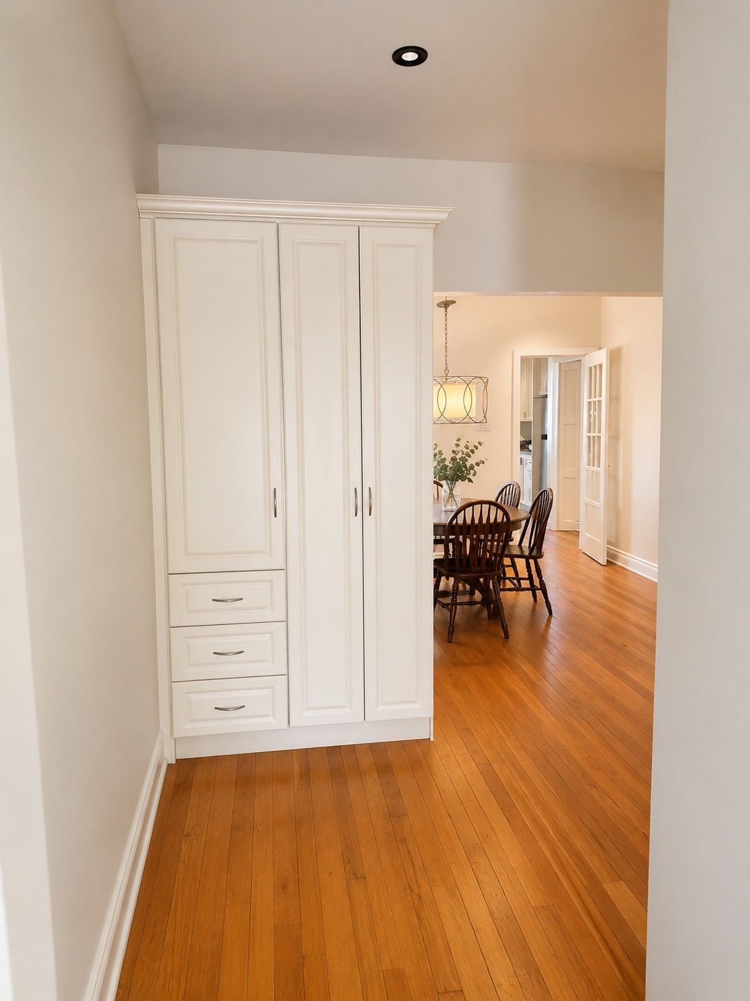 Una habitación con piso de madera, armario blanco y un comedor con sillas y una mesa.