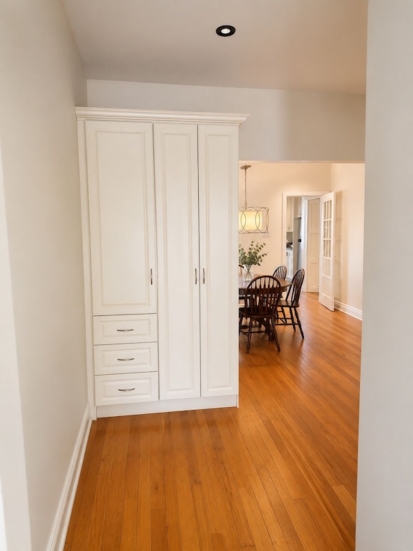 A room with a wooden floor, white wardrobe, and a dining area with chairs and a table.