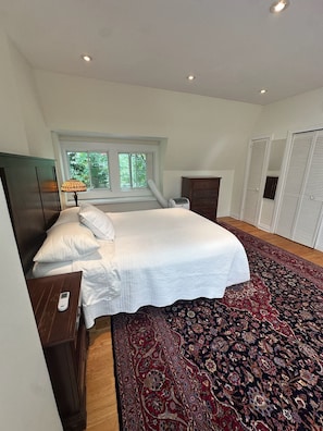 A bedroom with a bed, bedside table, lamp, window, radiator, wardrobe, and a patterned carpet.