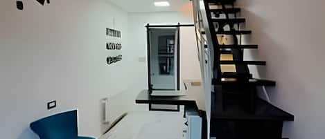 A modern interior with a staircase, a seating area with chairs, and a wall with text.
