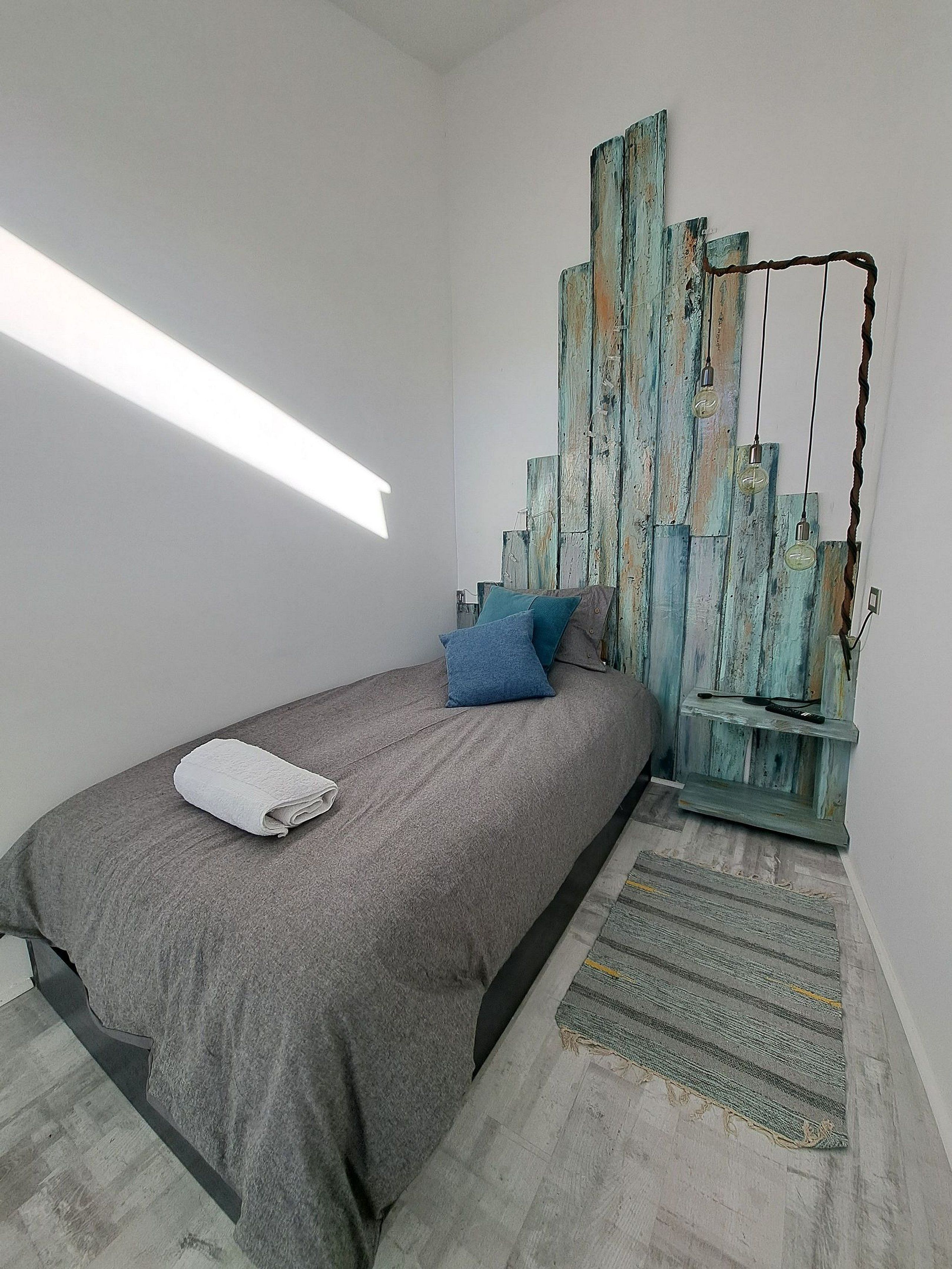 A bedroom with a bed, pillows, a wall-mounted light fixture, and a rug.