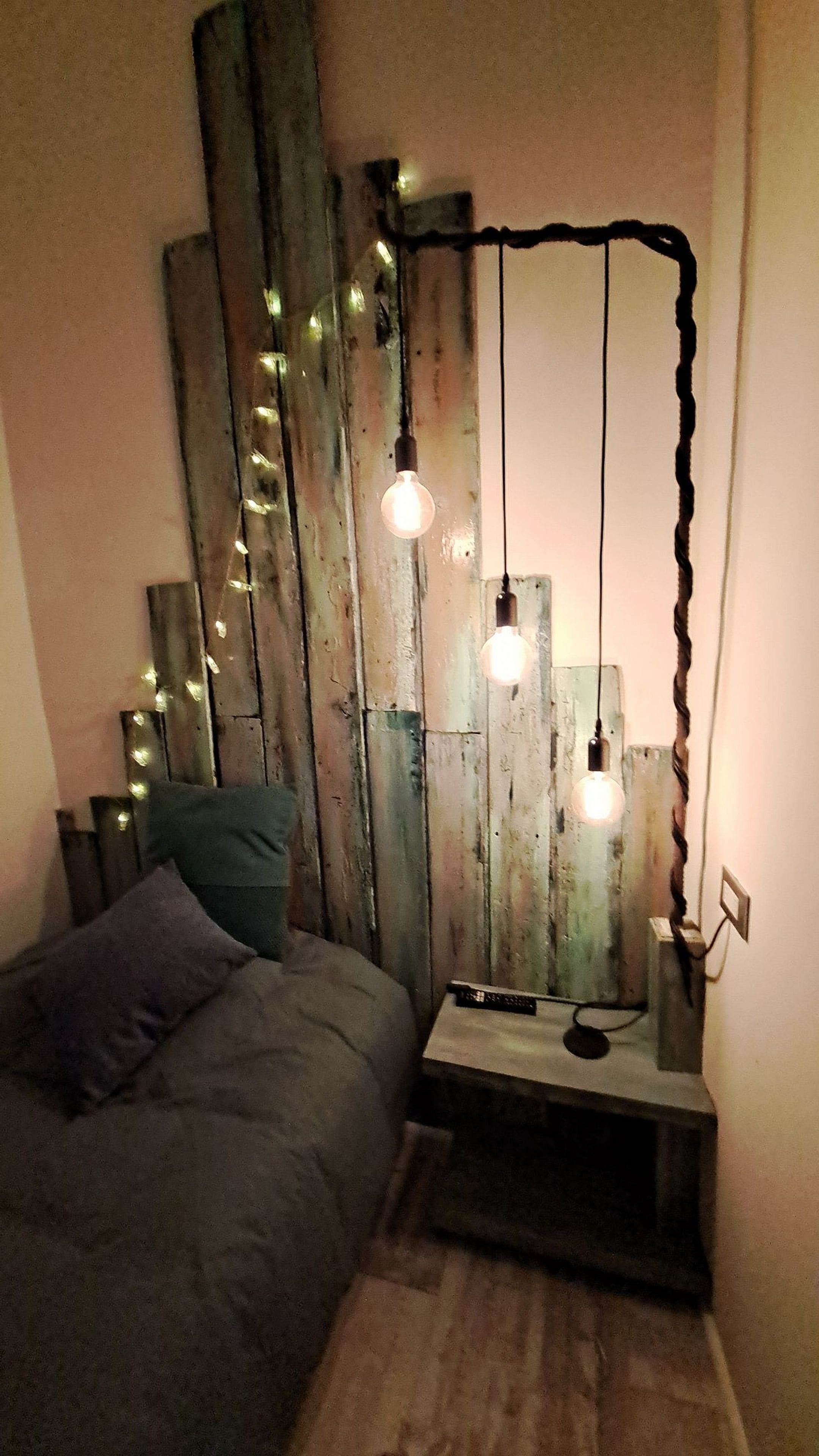 A bedroom with a bed, bedside table, and a wooden wall with hanging lights.