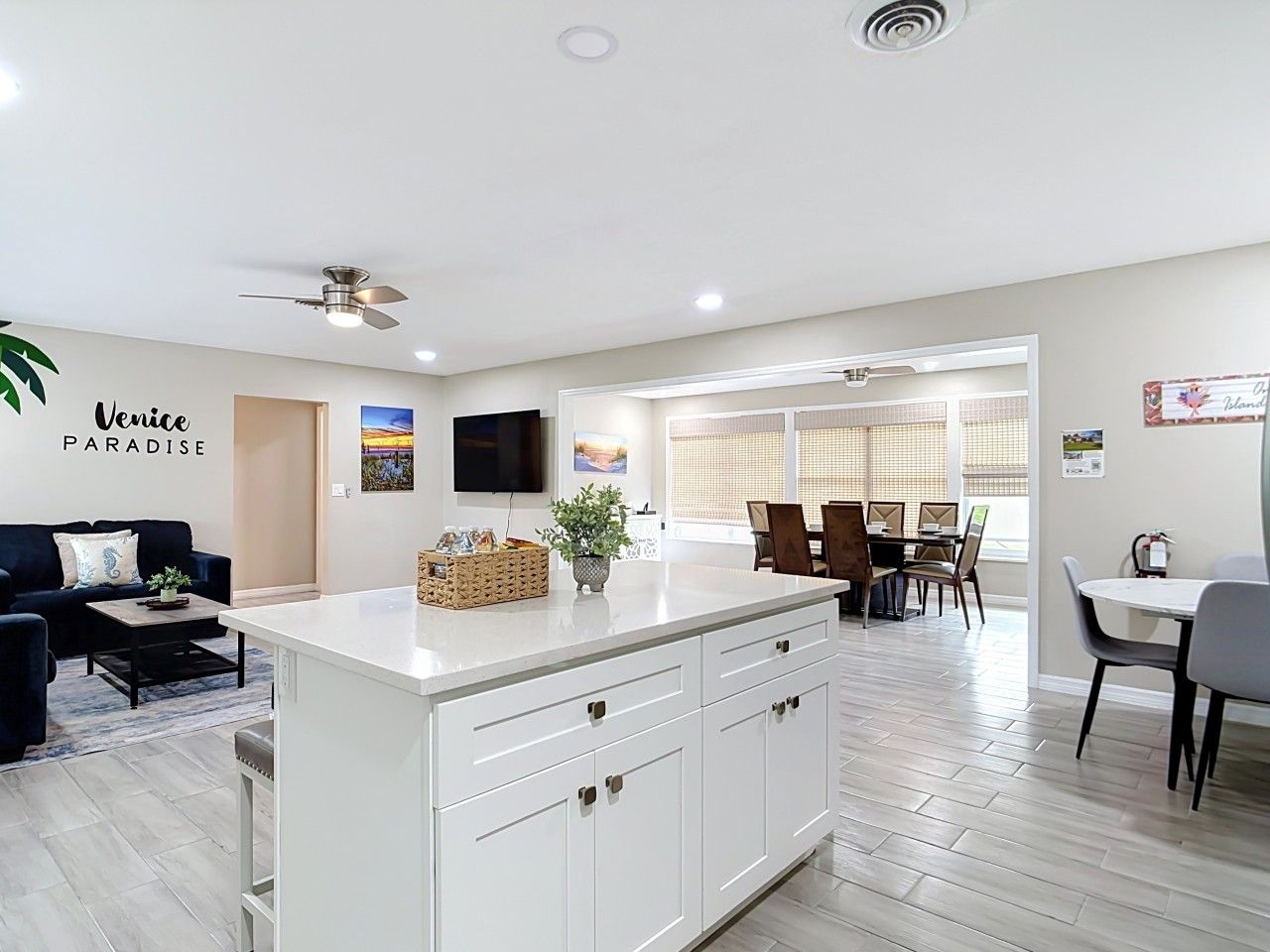 A modern kitchen with a white island, a dining area with a table and chairs, and a living room with a sofa and a TV.