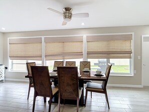 A dining area with a table set for six, a ceiling fan, and large windows with blinds.