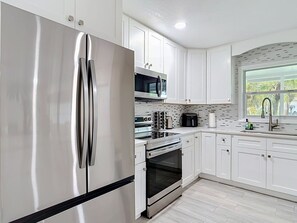 A modern kitchen with stainless steel appliances, white cabinetry, and a window providing natural light.