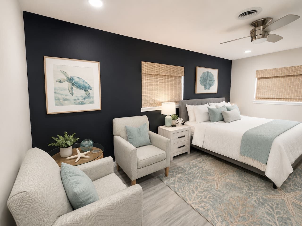 Un dormitorio con cama, dos sillas, una mesita de noche, una lámpara de pared y un ventilador de techo.
