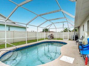 Ein überdachter Pool im Freien mit Metallgestell, eine Terrasse mit Tisch und Stühlen sowie ein weißer Zaun im Hintergrund.