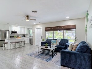 A modern living room with a dark blue sofa, a coffee table, and a kitchen area with white cabinets and a microwave.