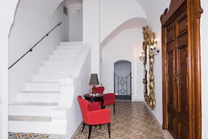 A hallway with a white staircase, a red chair, a small table with a lamp, and a decorative mirror. - Villa Evia by My Villa Collection (Positano)