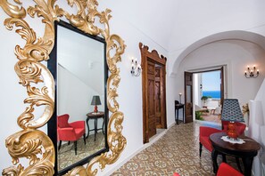 A hallway with a large ornate mirror, red chairs, a patterned floor, and a view of the sea through an open door. - Villa Evia by My Villa Collection (Positano)
