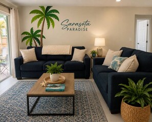 Ett vardagsrum med två mörka soffor, ett soffbord och en vägg prydd med en palm och en skylt med texten ”Sarasota Paradise”.