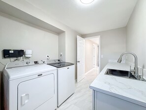 A laundry area with a washing machine and dryer, a sink with a modern faucet, and a hallway leading to another room.