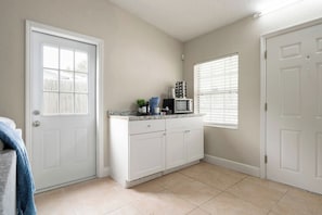 A kitchen with white cabinets, a countertop, a microwave, and a window with blinds.