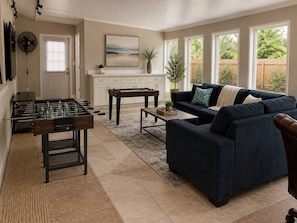 A living room with a foosball table, a sofa, a coffee table, and a view of the outdoors through large windows.