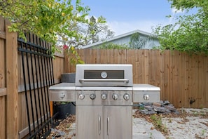 A stainless steel outdoor grill with four burners, a control panel, and a cabinet below.