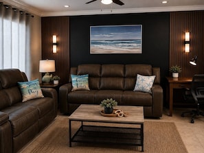 A living room with two brown leather sofas, a wooden coffee table, a ceiling fan, and a framed ocean view painting.