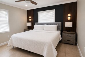 Un dormitorio con una cama grande, dos mesitas de noche, un ventilador de techo y lámparas fijadas a la pared.