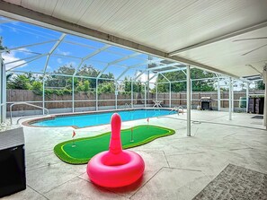 An outdoor swimming pool area with a covered patio, a red inflatable object, and a green artificial turf. - AMI Coastal Retreat Heated Pool 4BR 2BA Sleep 12 (Bradenton)